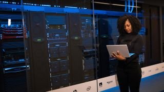 Woman using laptop in front of servers