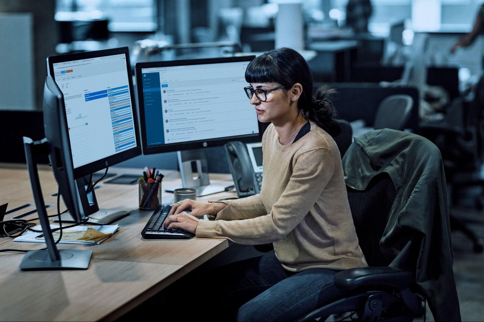 Brunette woman sitting at a desk with multiple computer screens