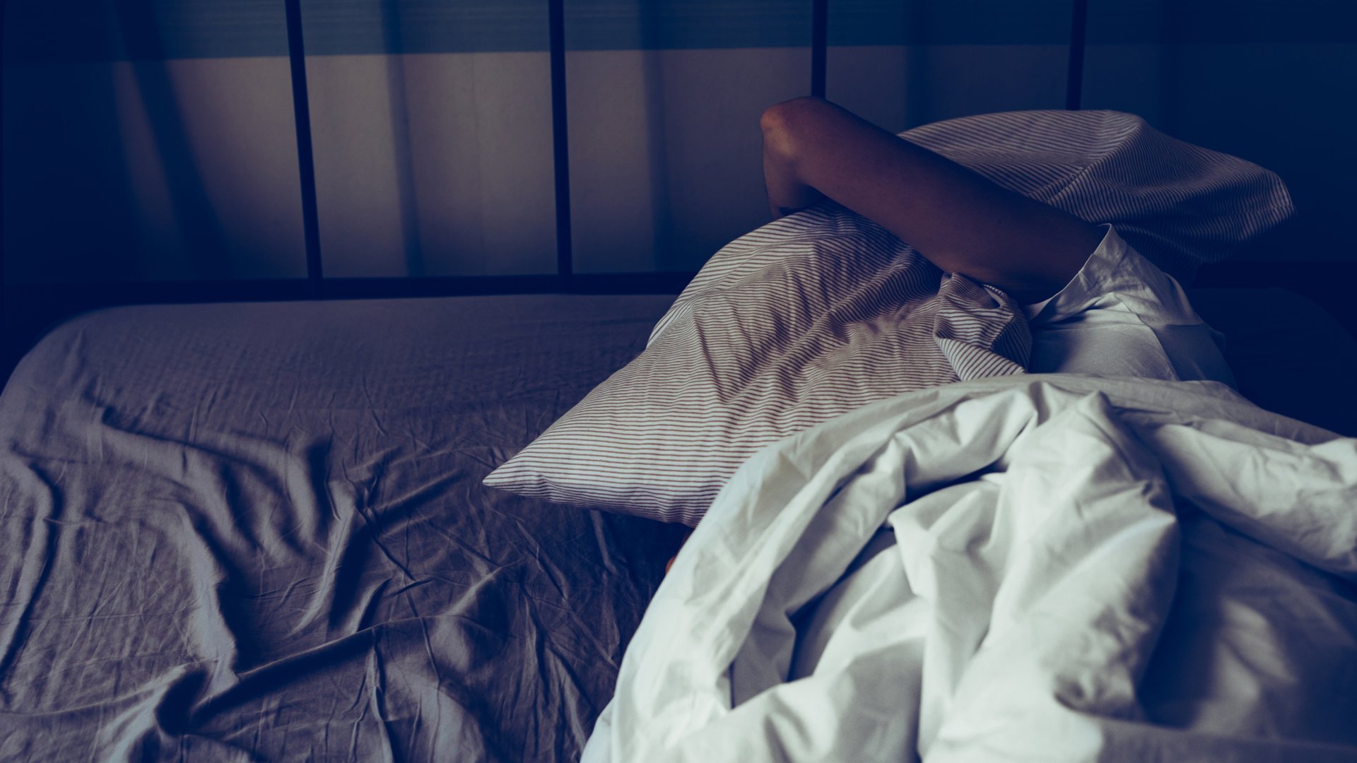 Eine Frau wacht nachts auf und legt sich frustriert, weil sie nicht schlafen kann, ein Kissen über den Kopf