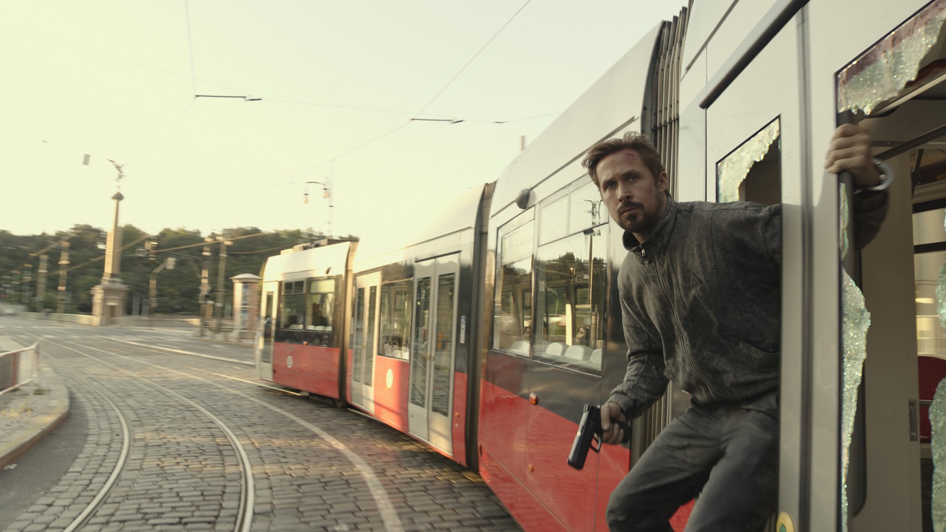 Ryan Gosling's Sierra Six strapped to the side of a train, gun drawn, in The Gray Man