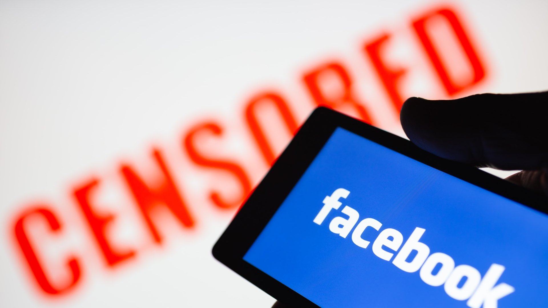 Téléphone intelligent en main montrant le logo Facebook. Texte censuré rouge flou sur fond
