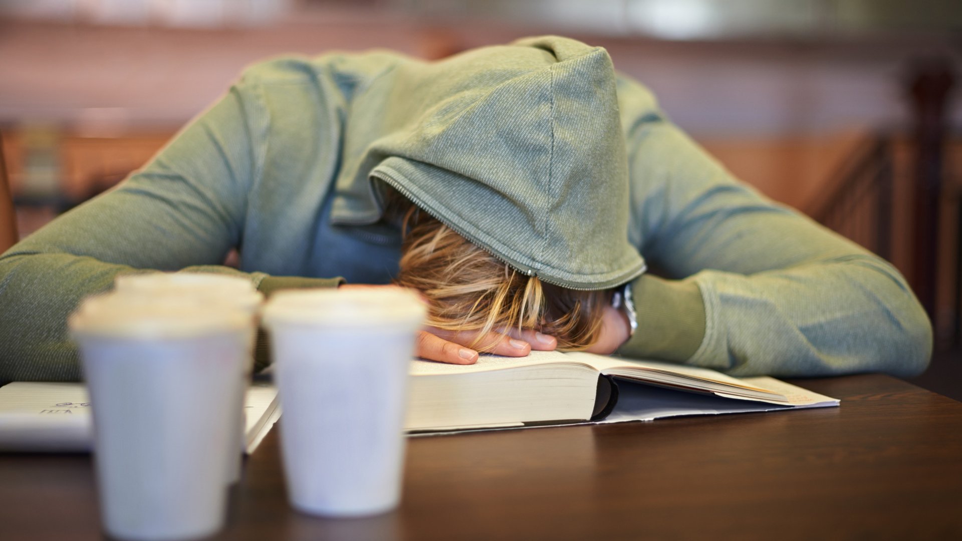 Ein Schüler in einem grauen Kapuzenpulli schläft im Unterricht ein