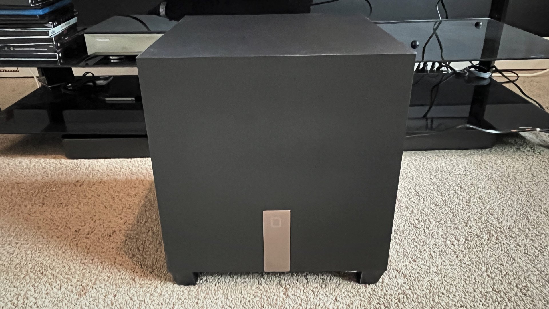 Mini caisson de basses barre de son Definitive Technology Studio 3D devant un meuble TV sur un tapis blanc