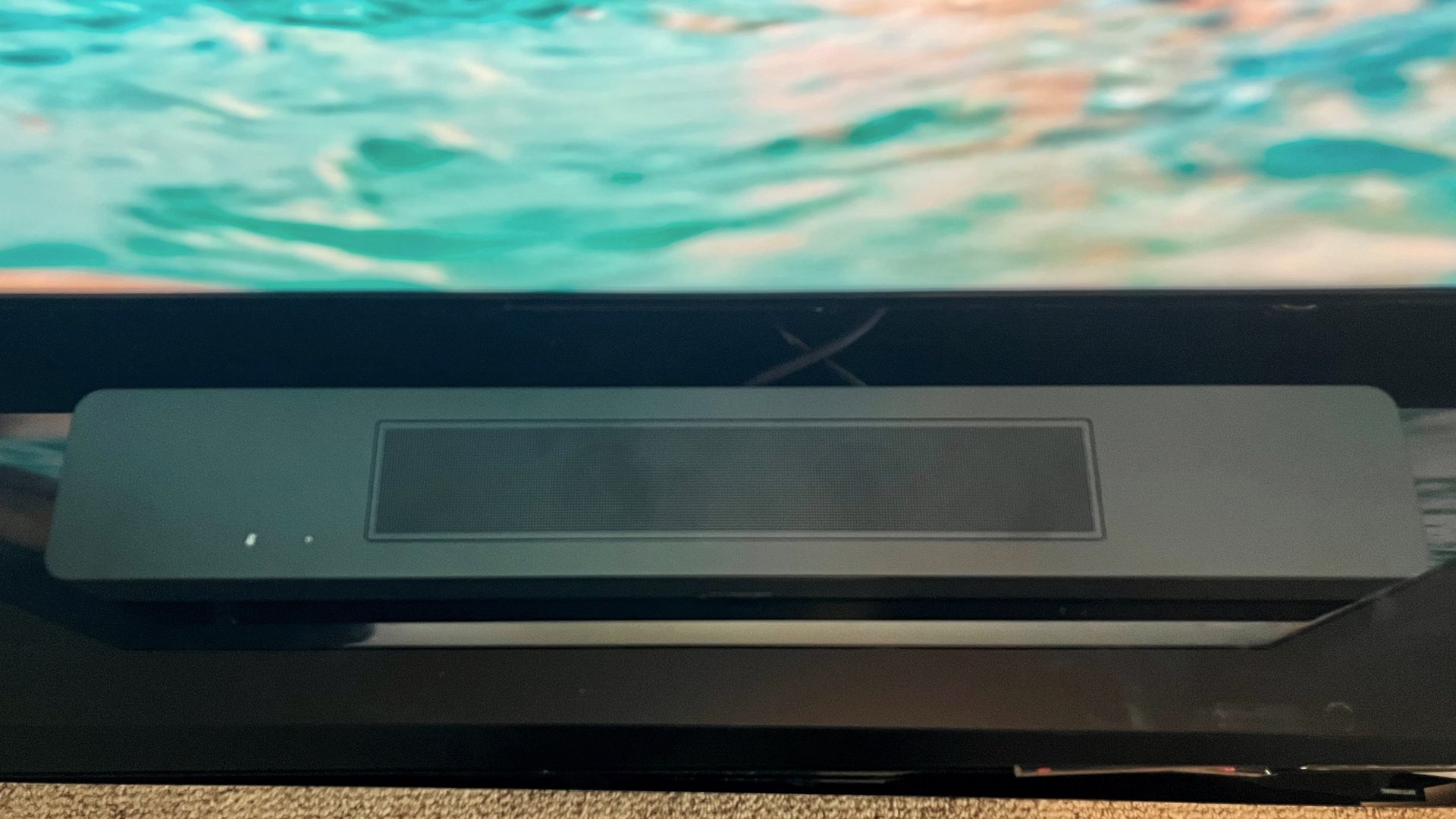 Bose Soundbar 600 på TV-bänk med blå skärm i bakgrunden